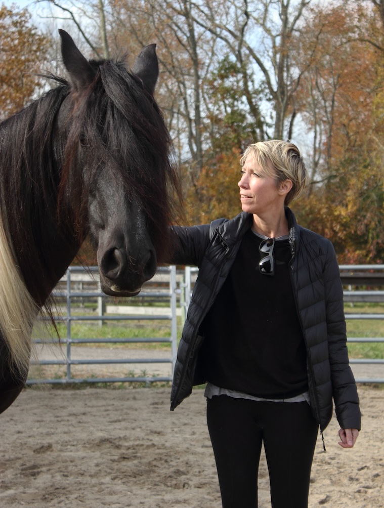 A woman standing in an outdoor round pen, touching the side of a horse